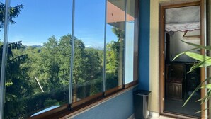 A balcony with a clear view of a forested area, a trash bin, and a glimpse of a kitchen area. - Vivienda Vacacional La Casa Azul ll (Ceceda)