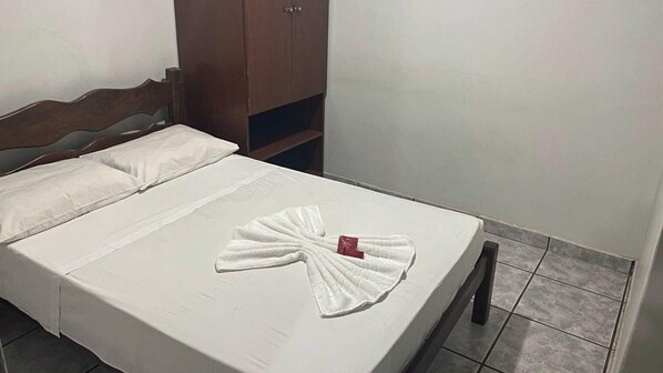 A neatly made bed with a towel arranged in a fan shape, a wooden wardrobe, and tiled flooring. - Carlton Imbiara Express (Araxá)