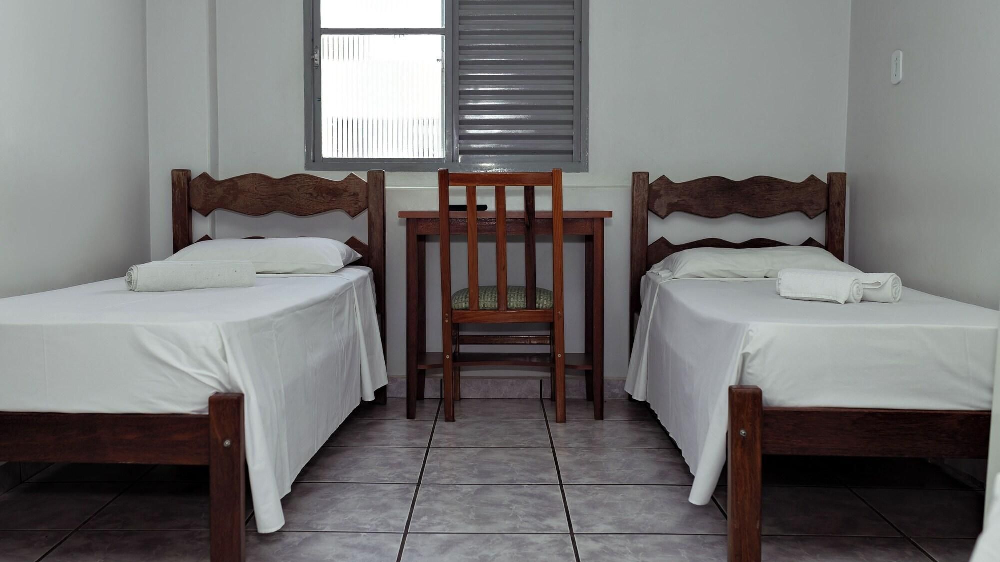 A room with two wooden beds, a small table, and a chair.