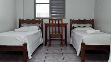 Um quarto com duas camas de madeira, uma mesinha e uma cadeira.