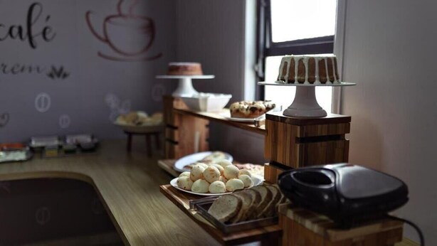 A breakfast buffet with various pastries and bread, a cake on a stand, and a coffee machine. - Carlton Imbiara Express (Araxá)