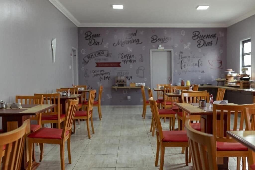 Un restaurante con mesas y sillas de madera, una zona de cocina y una pared decorada con frases y dibujos.