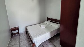 A small, clean room with a single bed, a wooden nightstand, and a door. - Carlton Imbiara Express (Araxá)