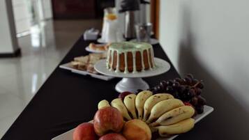 A table with a cake, fruits, and a coffee machine.