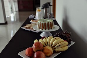 A table with a cake, fruits, and a coffee machine. - Carlton Imbiara Express (Araxá)
