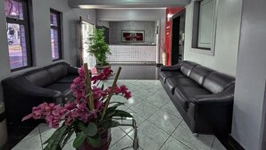 A reception area with two black leather sofas, a potted plant, and a tiled floor. - Carlton Imbiara Express (Araxá)