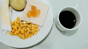 A plate with scrambled eggs, toast with jam, a slice of bread, and a half-cut fruit, accompanied by a cup of black coffee. - Hotel Verde Mares (Macapa)