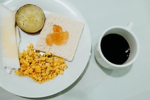 Un plato con huevos revueltos, tostadas con mermelada, una rebanada de pan y media fruta, acompañado por una taza de café negro.