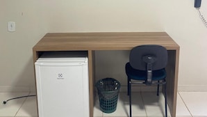 A compact room with a wooden desk, a small white refrigerator, a trash bin, and a chair. - Hotel Verde Mares (Macapa)
