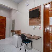 Quarto pequeno com escrivaninha, cadeira e televisão fixada na parede.