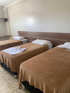 Una habitación de hotel con dos camas, cada una con una manta marrón y almohadas blancas. Hay una mesita con un control remoto y una toalla blanca.