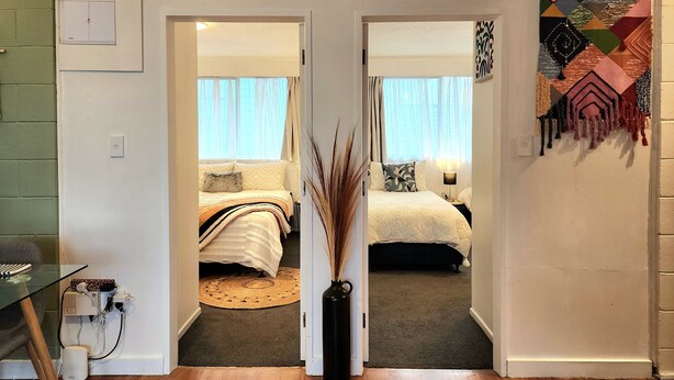 Een gang die leidt naar twee slaapkamers, elk met een bed, nachtkastje, lamp en een kunstwerk aan de muur.