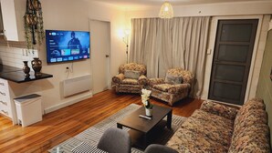 Een woonkamer met een bank, twee fauteuils, een salontafel en een aan de muur bevestigde televisie.
