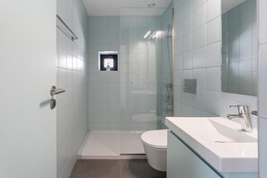 A modern bathroom with a glass shower enclosure, a white toilet, and a glass-fronted sink. - GuestReady - One lovely studio in downtown (Porto)
