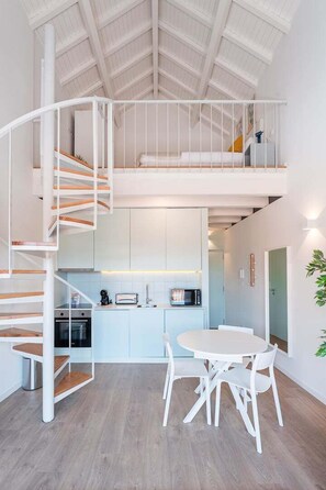 A modern interior with a spiral staircase leading to a loft bedroom, a kitchen with white cabinets, and a dining area with a round table and chairs. - GuestReady - One lovely studio in downtown (Porto)