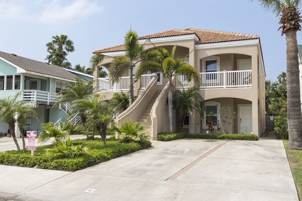 A two-story building with a beige exterior, a white balcony, and a curved staircase leading to the second floor.