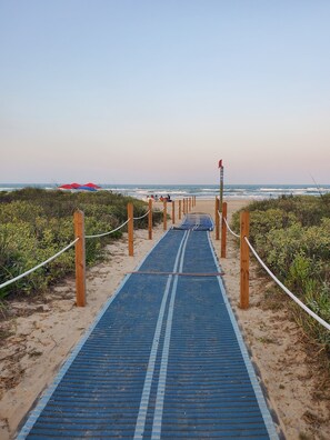 A beach path leading to the ocean with a blue mat and wooden posts.