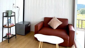 A modern living room with a red sofa, a white coffee table, and a grey cabinet. There is a window with a view of greenery and a white wall with a textured pattern. - Rai Rak Doi Phutubberk (Lom Kao)