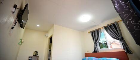 A bedroom with a bed, a TV mounted on the wall, a ceiling fan, and a window with curtains.