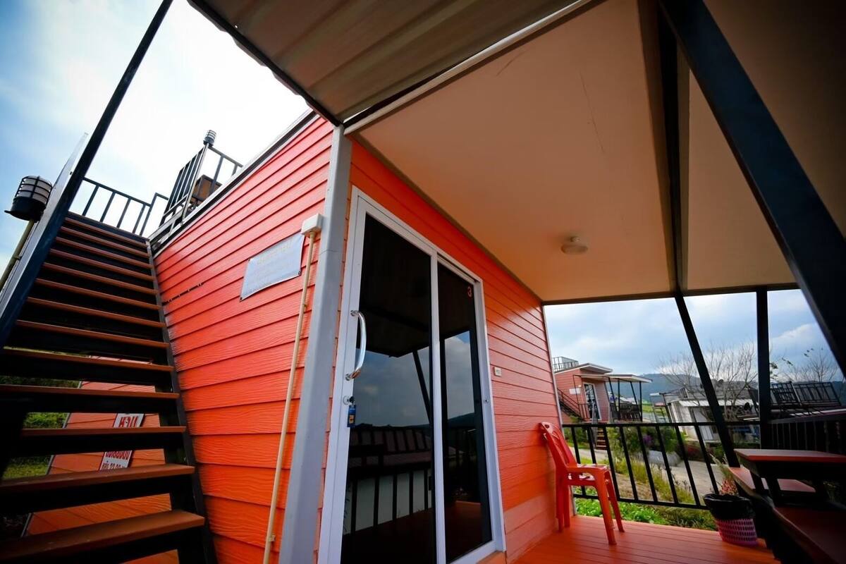 A red building with a sliding glass door, a staircase, and a covered outdoor area with a table and chairs.