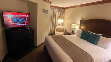 A hotel room with a bed, a TV on a dresser, a lamp, and a window with curtains.