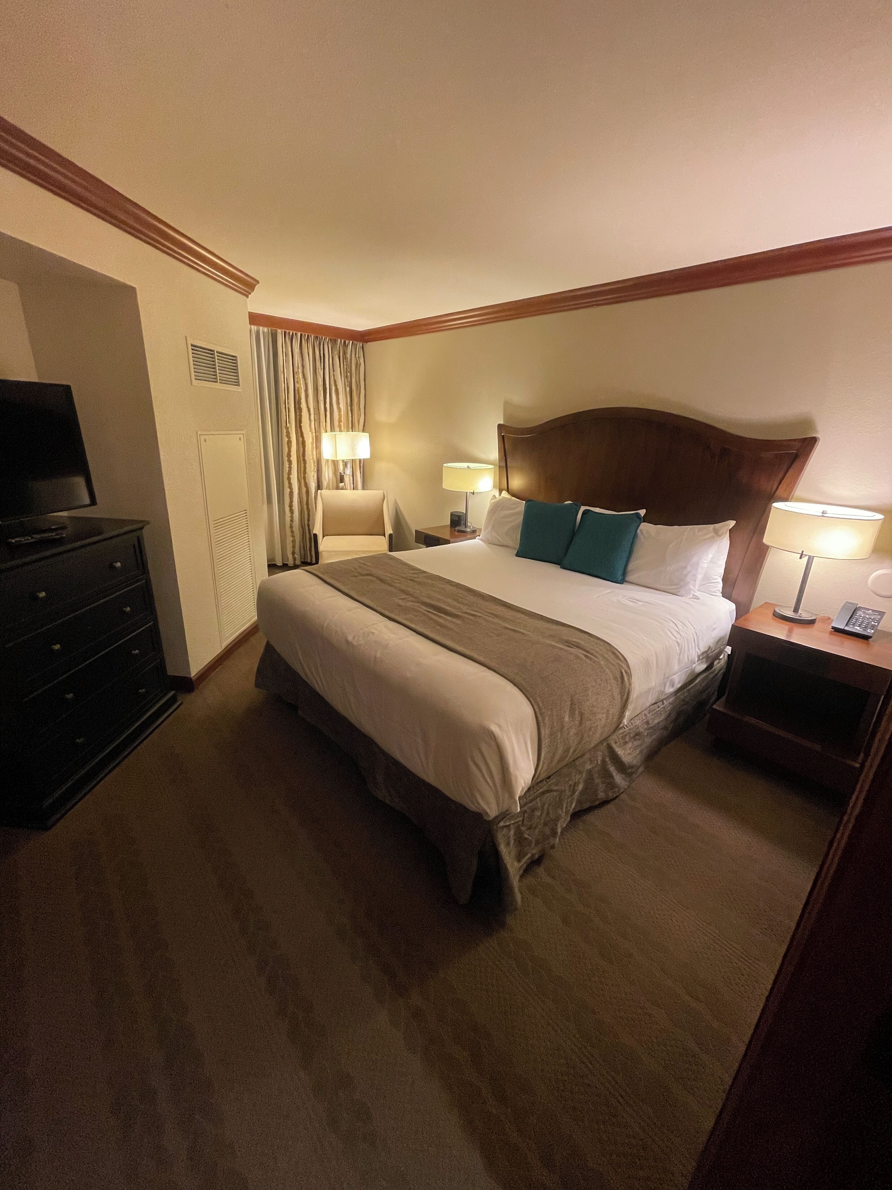 A hotel room with a large bed, a TV, a dresser, and two bedside lamps.