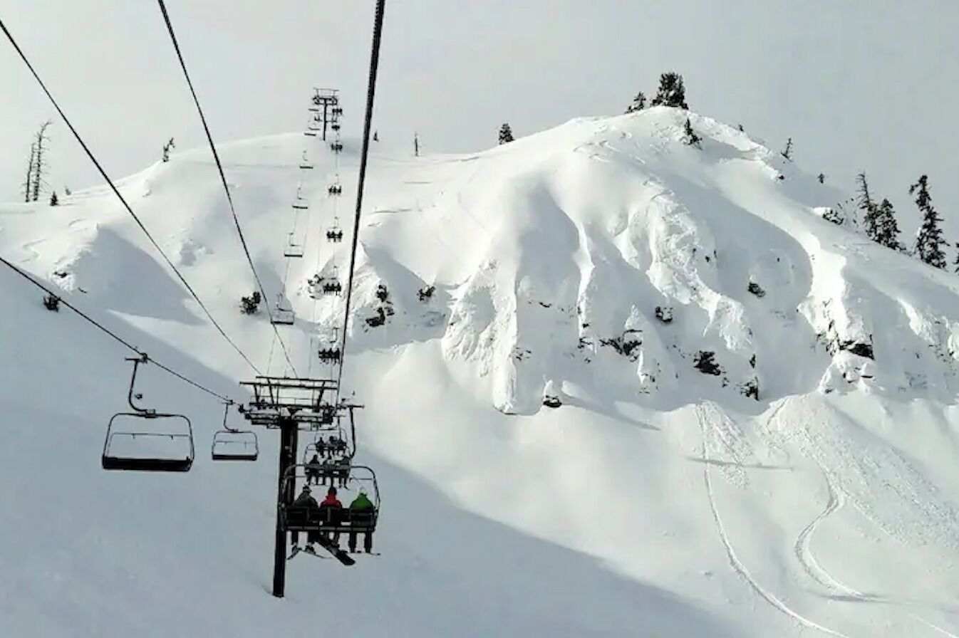 A ski lift with chairs moving up a snowy mountain slope.