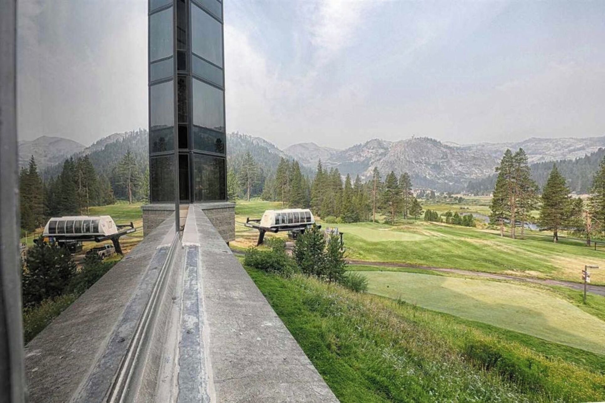 A modern building with a glass facade and a view of a golf course and mountains in the background.