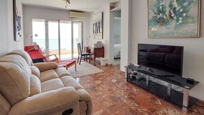 Un salon avec un canapé beige, un téléviseur à écran plat et un coin repas comprenant une table et des chaises.