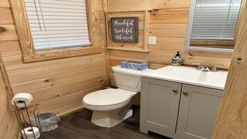 Baño de cabaña de madera pequeña con inodoro, lavamanos y un letrero que dice 'Agradecido, agradecido, bendecido'.