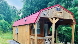 Een houten hut met een rood dak, een veranda en een grindpad.