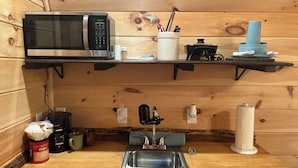 Een keuken met een magnetron, een spoelbak, een koffiezetapparaat en een pot Folgers Vanilla.