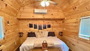 Een knus slaapkamer in een houten chalet, met een bed, een dressoir en een plafondventilator.