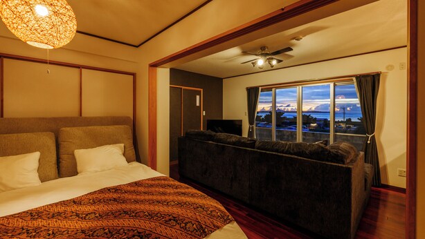 Ein Schlafzimmer mit einem großen Bett, einer Couch, einem Deckenventilator und Blick ins Freie.