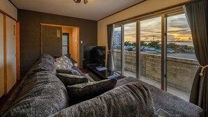 Ein modernes Wohnzimmer mit einer großen Couch, einem Fernseher und einem Balkon mit Blick auf die Stadt.