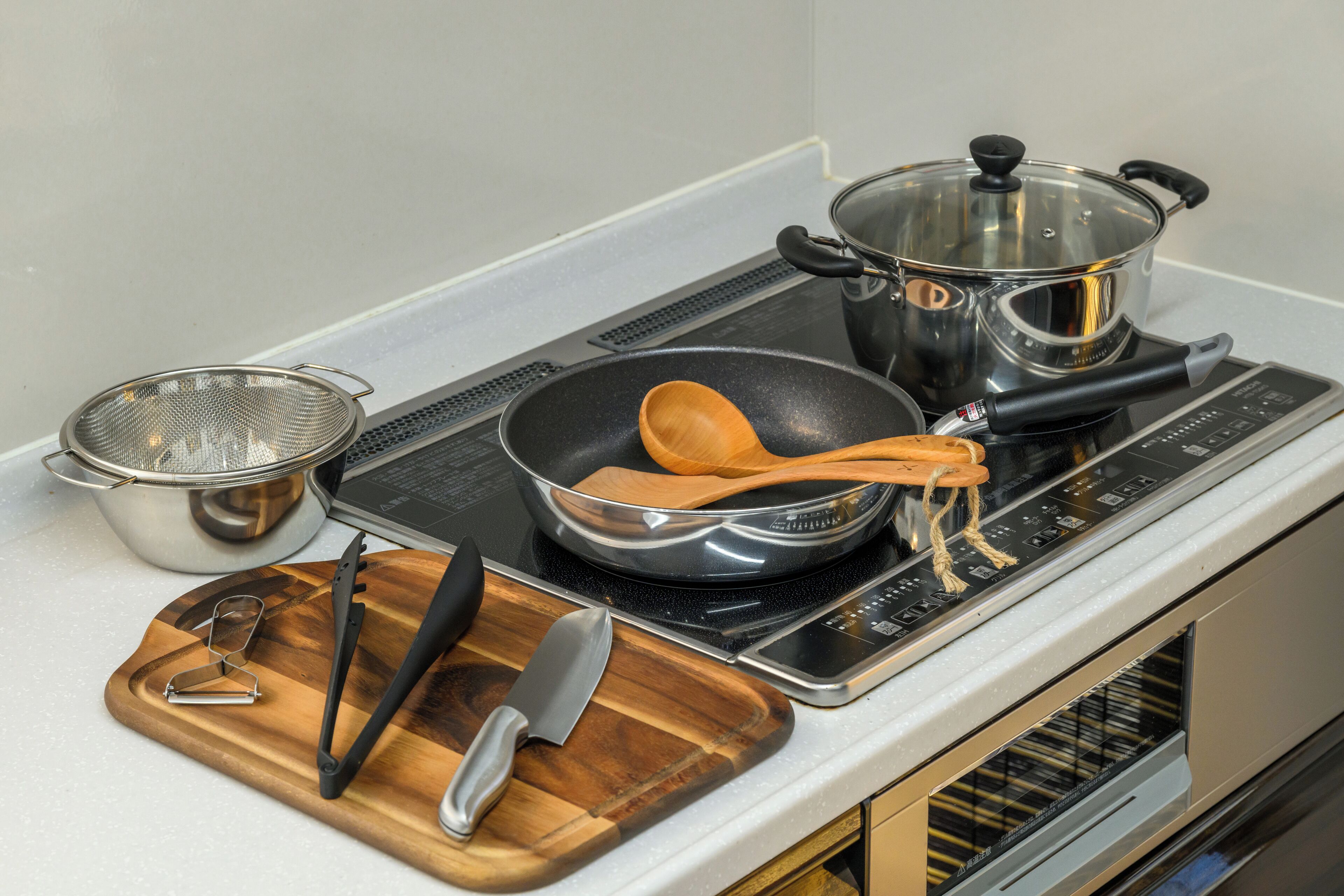 Une cuisine équipée d’une cuisinière, de casseroles, d’une poêle, d’ustensiles en bois, d’une passoire et d’une planche à découper avec un couteau et un outil en métal.