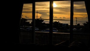 Blick durch ein Fenster auf einen Sonnenuntergang, eine Brücke und parkende Autos.