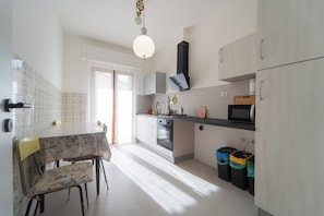 A kitchen with a dining table, chairs, a microwave, and trash bins. - Colle di Perugia - cozy apartment in villa (San Martino In Colle)