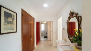 Un corridoio con una porta in legno, un quadro incorniciato, uno specchio e una scrivania con documenti e un vaso di fiori.