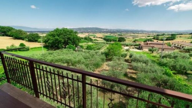 Un balcone con vista su un paesaggio rurale, tra campi e alberi.