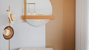 Ein modernes Badezimmer mit rundem Spiegel, Pendelleuchten, einer Wandverkleidung aus Holz und einer weißen Sitzbank.