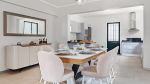 A modern dining area with a wooden table set for four, surrounded by chairs. A kitchen is visible in the background with a stove and cabinets. - Glimpse of the City by Homie (Funchal)