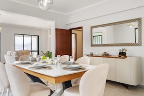 A dining area with a wooden table set for six, surrounded by chairs. A white cabinet with a mirror and decorative items is against the wall. - Glimpse of the City by Homie (Funchal)