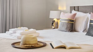 Ein ordentlich bezogenes Bett mit Kissen, einem Hut und einem Buch in einem Hotelzimmer.