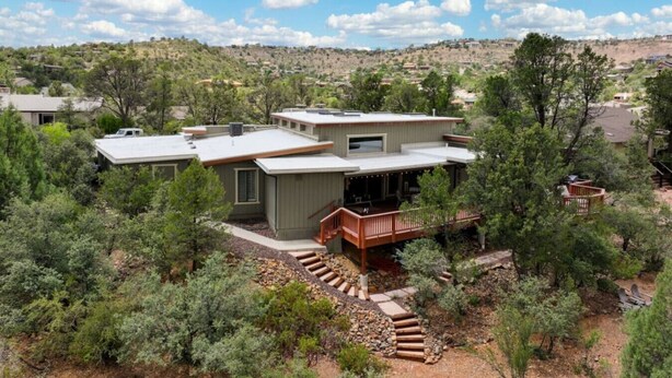 Une maison moderne à deux étages, dotée d’une terrasse et entourée d’une végétation luxuriante et d’arbres.
