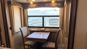 Een compact camperinterieur met een eethoek, een raam met uitzicht op een ander voertuig en een kleine kitchenette.