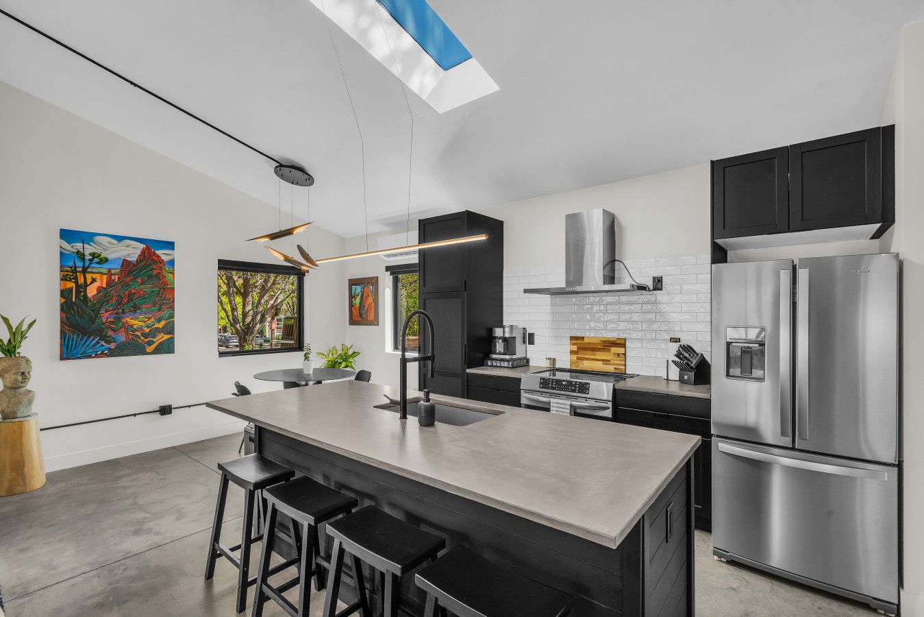 Een moderne keuken met een centraal eiland, roestvrijstalen apparatuur en kunstwerken aan de muur.
