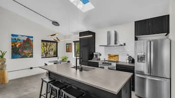 Een moderne keuken met een centraal eiland, roestvrijstalen apparatuur en kunstwerken aan de muur.