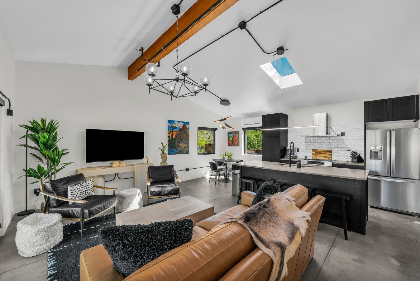 Ein modernes Wohnzimmer mit einer Couch, einem Couchtisch und einem Fernseher. Es gibt eine Küche mit Kühlschrank und Herd.