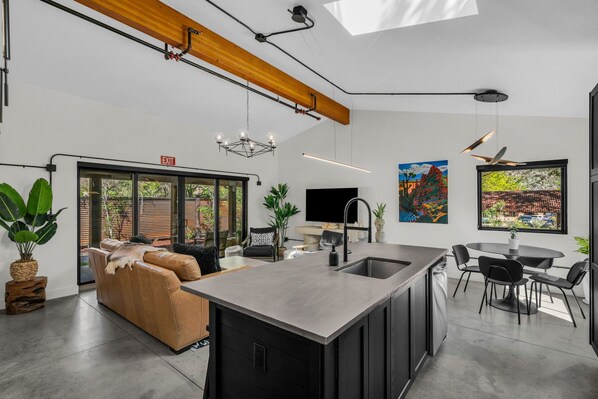 A modern kitchen with a central island, a dining area with a round table, and a seating area with a sofa.